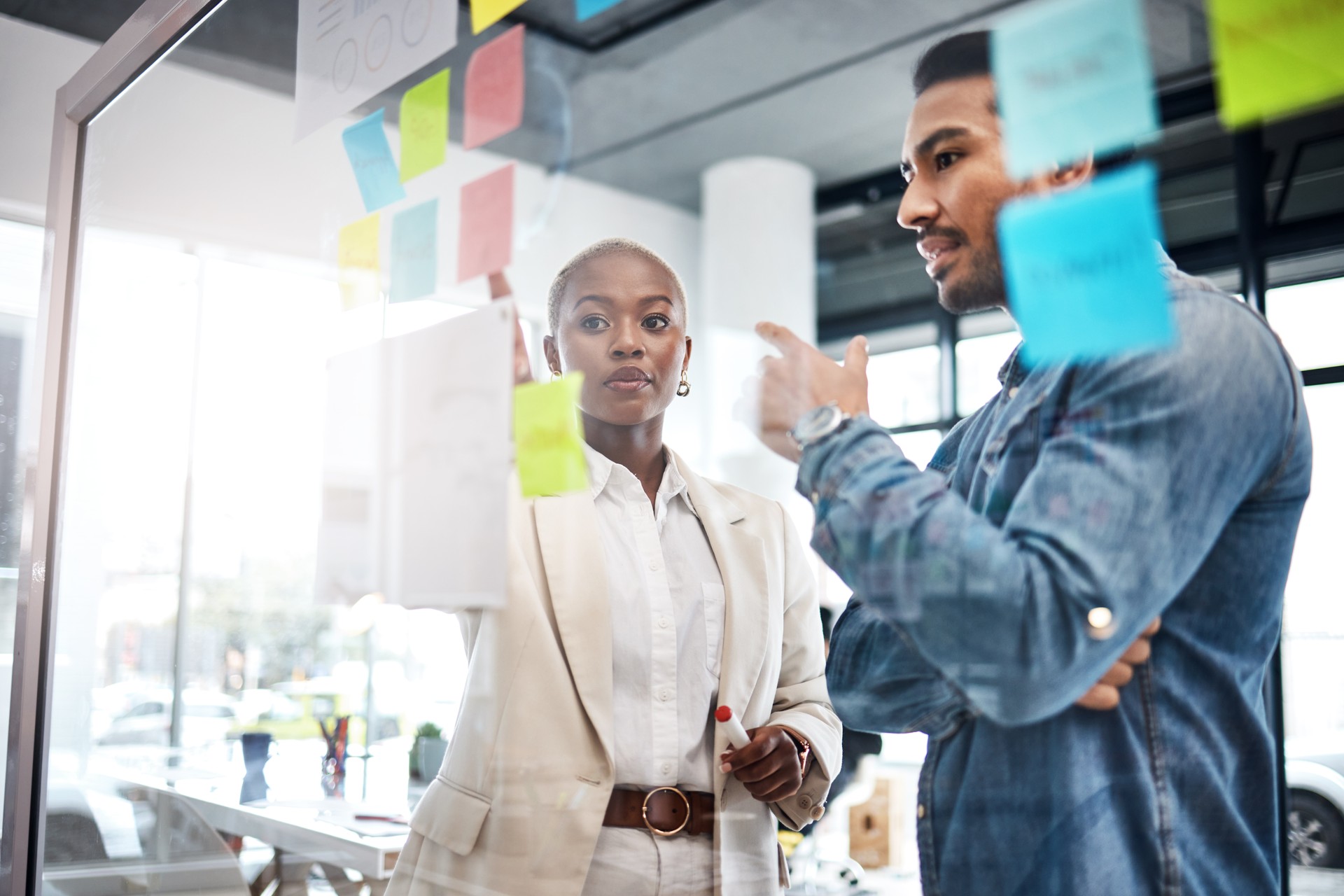 Creative people, thinking and meeting for schedule planning, brainstorming or team strategy at the office. Man and woman in teamwork decision for project plan, tasks or sticky note ideas in startup